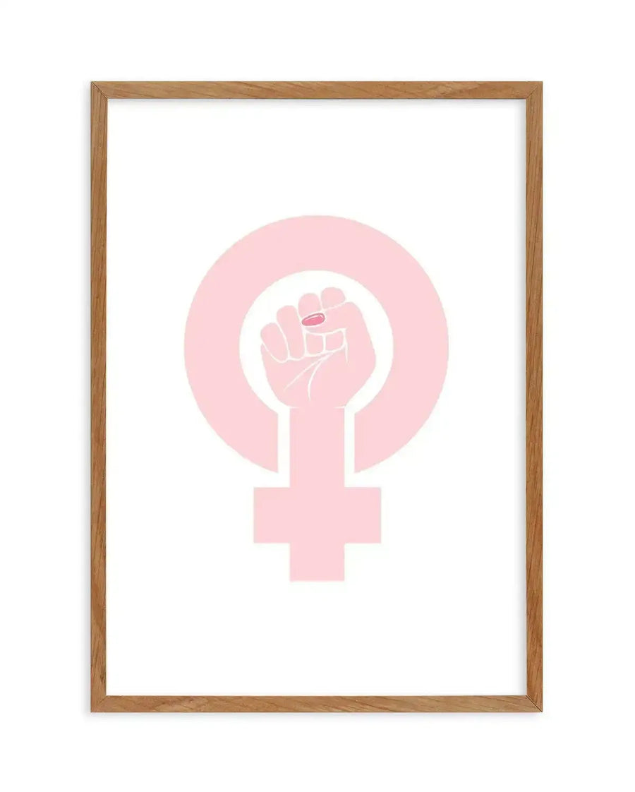 Art print featuring a pale pink female power symbol with a raised fist in the center, printed on fine art paper and displayed in a natural oak frame with white border.
