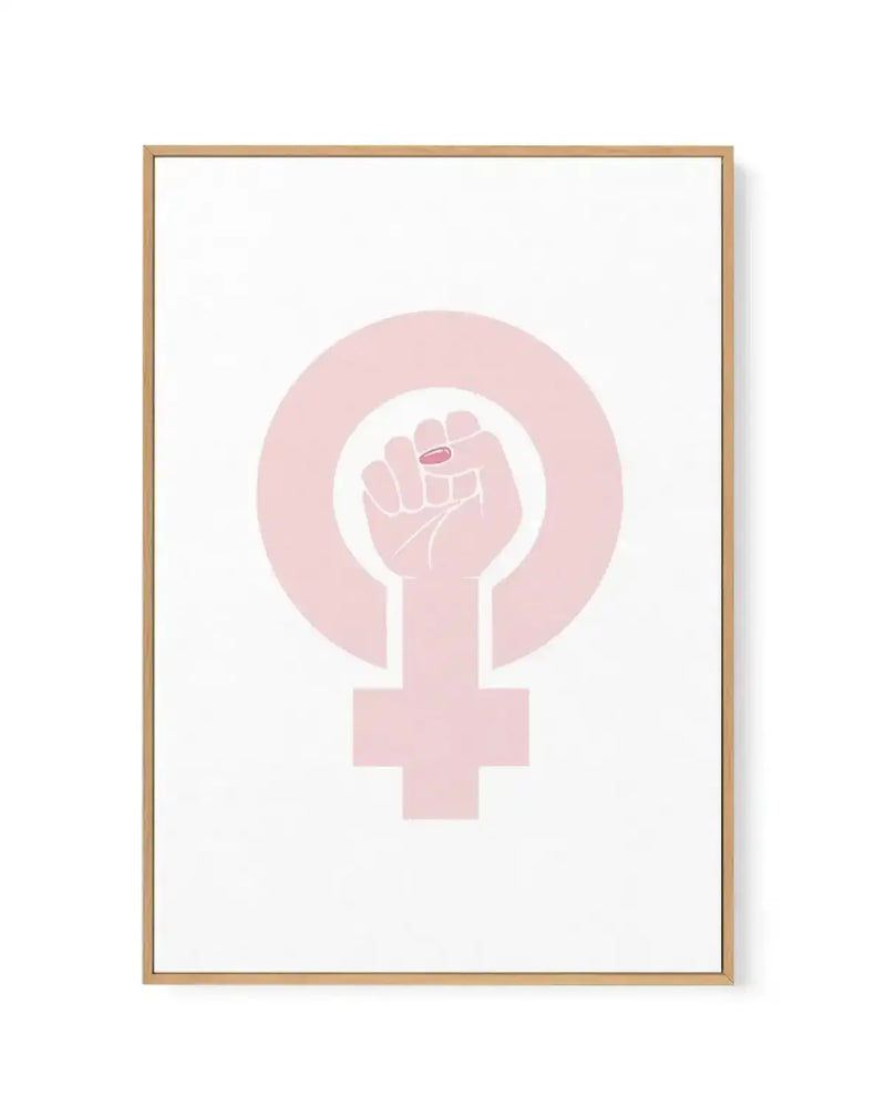Framed canvas art print featuring a feminist symbol in soft blush pink against a white background. The design shows a female gender symbol with a raised fist integrated into the circle at the top. The artwork is displayed in a natural wood frame with clean lines and a white border around the canvas.