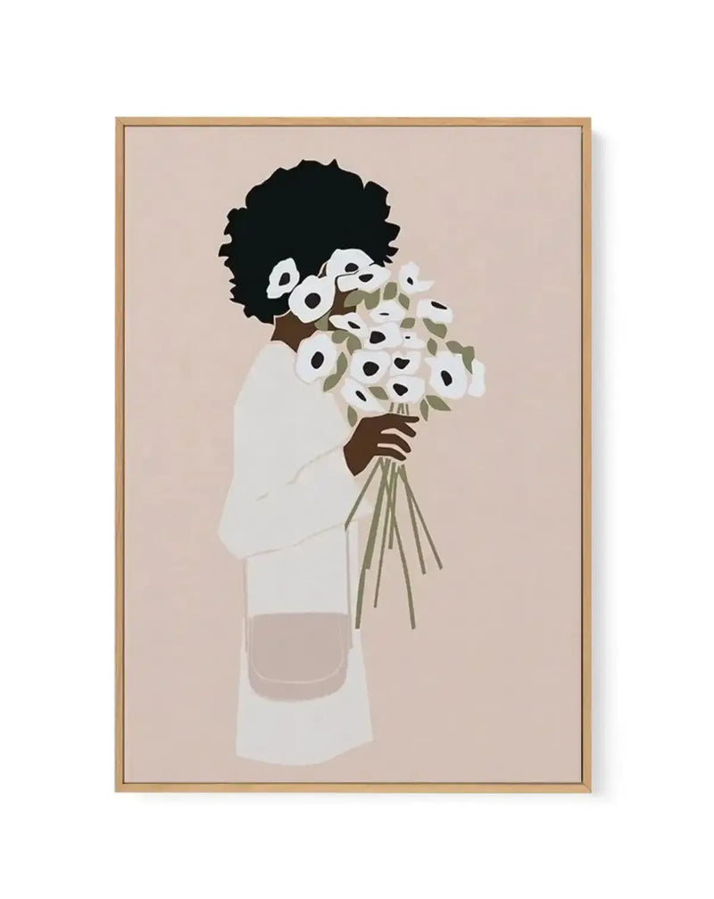 Framed canvas art print featuring a minimalist illustration of a figure with a voluminous black afro hairstyle wearing a cream-colored long-sleeved garment, holding a bouquet of white flowers with black centers and olive-green stems and leaves. The figure is shown from shoulders up against a soft beige background. The artwork uses a limited color palette of black, cream, white, olive green, and brown tones in a flat illustration style. The canvas is mounted in a natural wood frame with a white border.