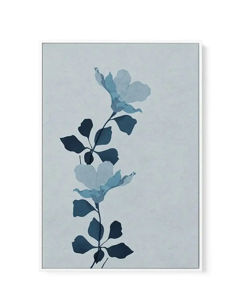 Framed canvas art print featuring a minimalist botanical illustration of flowering branches arranged vertically. The design shows layered foliage in varying shades of dark navy, teal, and light blue-grey against a pale grey-blue background. Delicate petals appear in lighter blue tones at the top and middle sections. The artwork has a soft, watercolor-like quality with subtle gradations. The canvas is set in a slim grey frame with a white border, creating a clean, contemporary presentation.