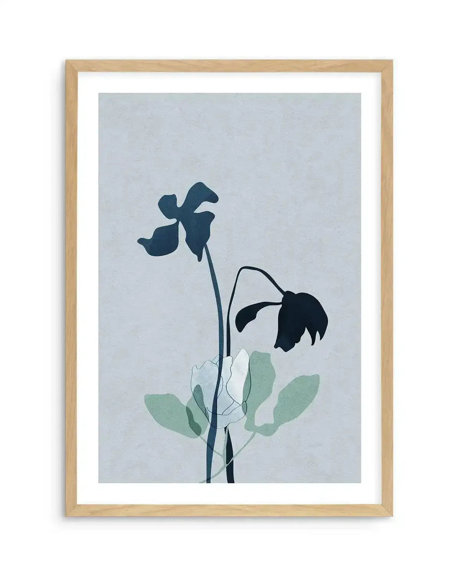 Framed art print titled "Fleur Graphique II" featuring two wilted flowers with dark navy silhouette petals against a soft pale blue background. Green watercolor-style leaves are visible at the base of the stems. The artwork has a minimalist aesthetic with organic, drooping flower forms. Natural wood frame with white border surrounding the print.
