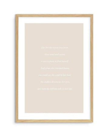 Art print featuring a poem in white serif font on a warm, pale beige background, displayed in a natural oak frame with white border. The poem reads: "For her the ocean was more than sand and water, it was a place to find herself. And when she returned home, you could see the wind in her hair, the endless dreams in her eyes, and taste the infinite salt on her lips."