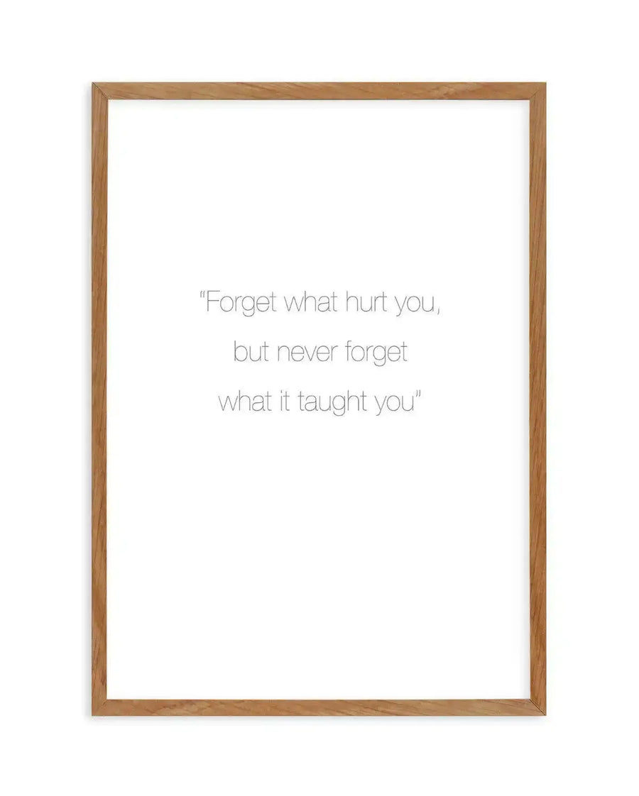 Art print featuring the quote "Forget what hurt you, but never forget what it taught you" in a simple, elegant grey font on a clean white background, displayed in a natural oak frame with white border.