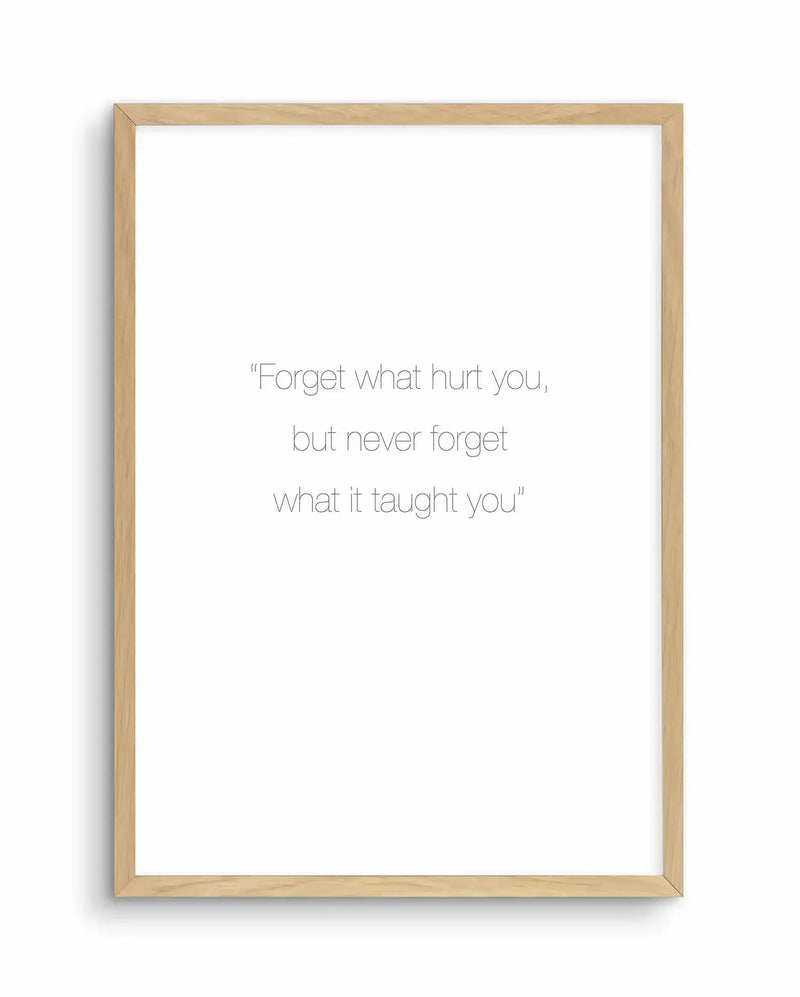 Art print featuring the quote "Forget what hurt you, but never forget what it taught you" in thin, sans-serif black font on a white background, displayed in a natural oak frame with white border.
