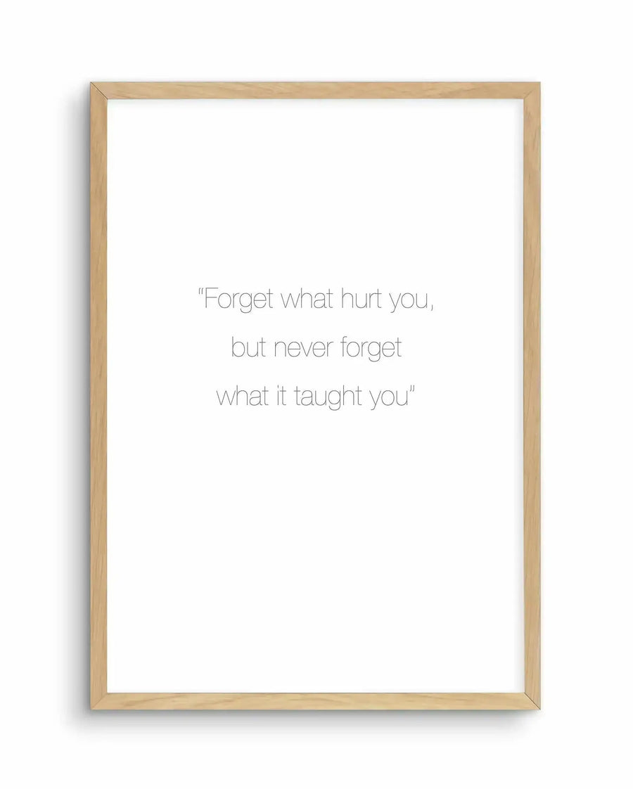 Art print featuring the quote "Forget what hurt you, but never forget what it taught you" in thin, sans-serif black font on a white background, displayed in a natural oak frame with white border.