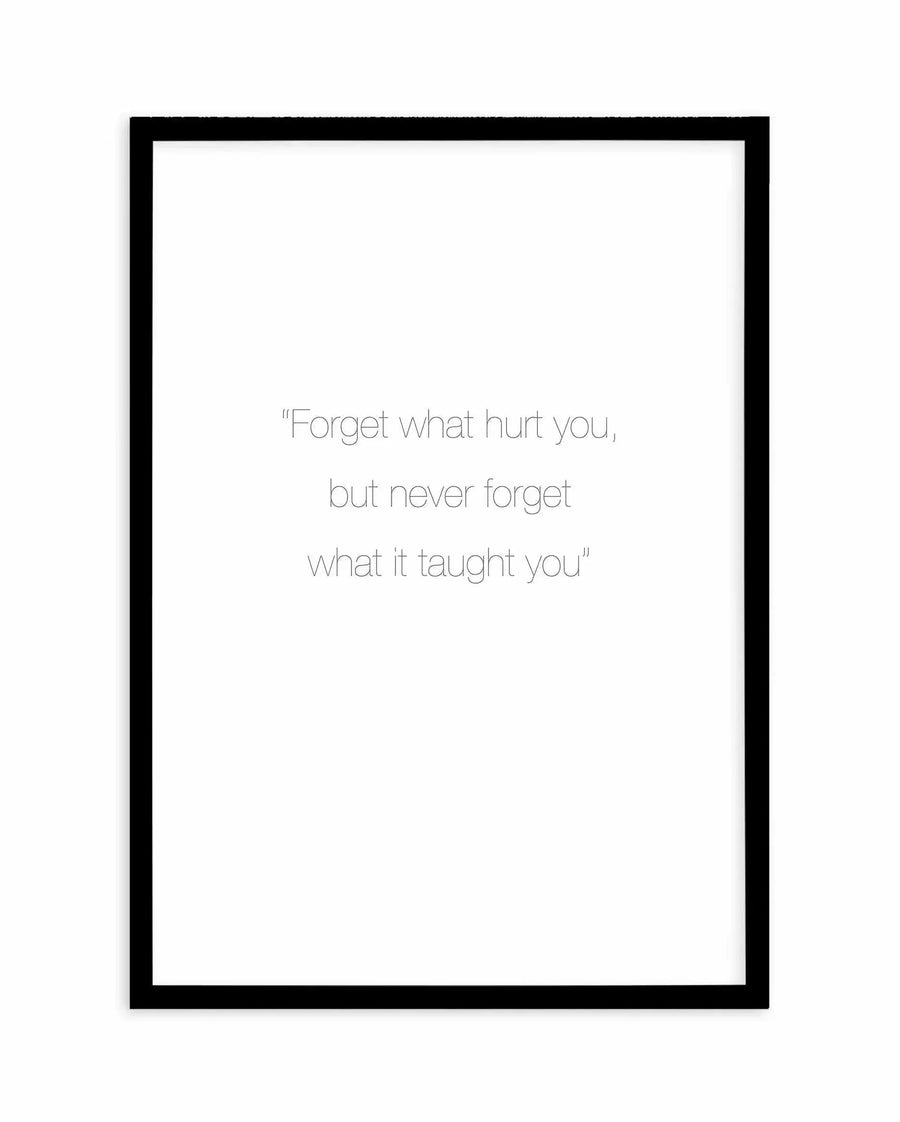 Art print featuring a motivational quote in thin, sans-serif black font on a crisp white background, displayed in a simple black frame with a white border. The quote reads: "Forget what hurt you, but never forget what it taught you".