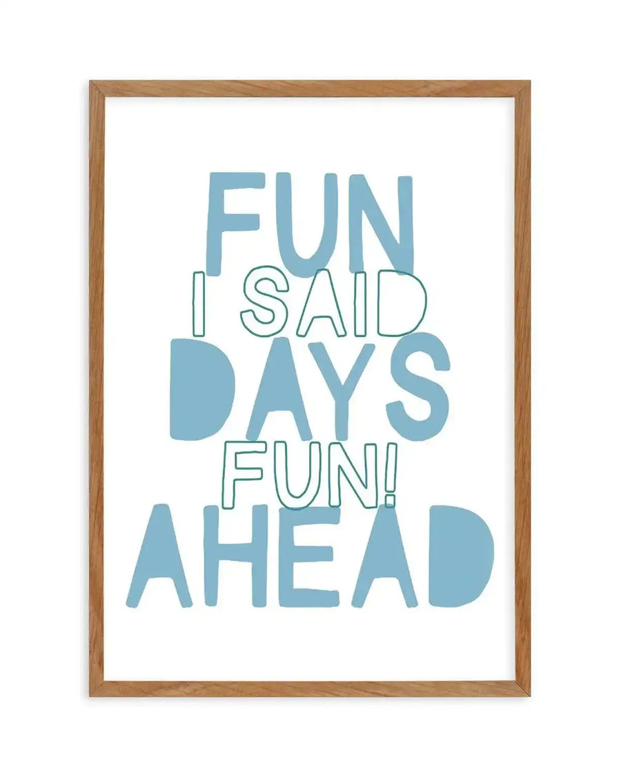 Framed art print with natural wood frame displaying typography design. Text reads "FUN I SAID DAYS FUN! AHEAD" in mixed font styles and weights. Letters in dusty blue and teal green create a playful, stacked composition on white background. Clean, modern illustration style with sans-serif typeface. White border surrounds the artwork within the wooden frame.