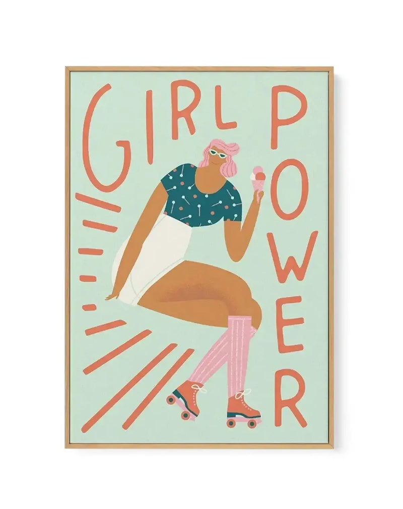 Framed canvas print featuring a vibrant illustration of a woman with pink hair and sunglasses, wearing a polka-dot top and white shorts, holding an ice cream cone, and sitting with roller skates on her feet. The words "GIRL POWER" are written in large, bold orange letters around her on a light mint green background, with a natural oak frame.
