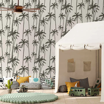 Lifestyle shot of a child's playroom featuring a white tent and a wallpaper with a repeating pattern of hand-drawn palm trees in charcoal black on a light cream background. The wallpaper features tall, slender palm trees with varying heights and frond shapes, creating a dense, tropical feel. The room includes a light green textured rug, various patterned pillows, toy cars, and a potted cactus.