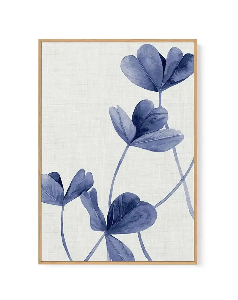 Framed canvas art print featuring three delicate blue flowers with open petals arranged vertically against a cream textured background. The flowers are rendered in watercolor style with varying shades of blue, from light periwinkle to deep indigo, with thin pale blue stems. The artwork is housed in a natural wood frame with a white border, creating a minimalist botanical composition.