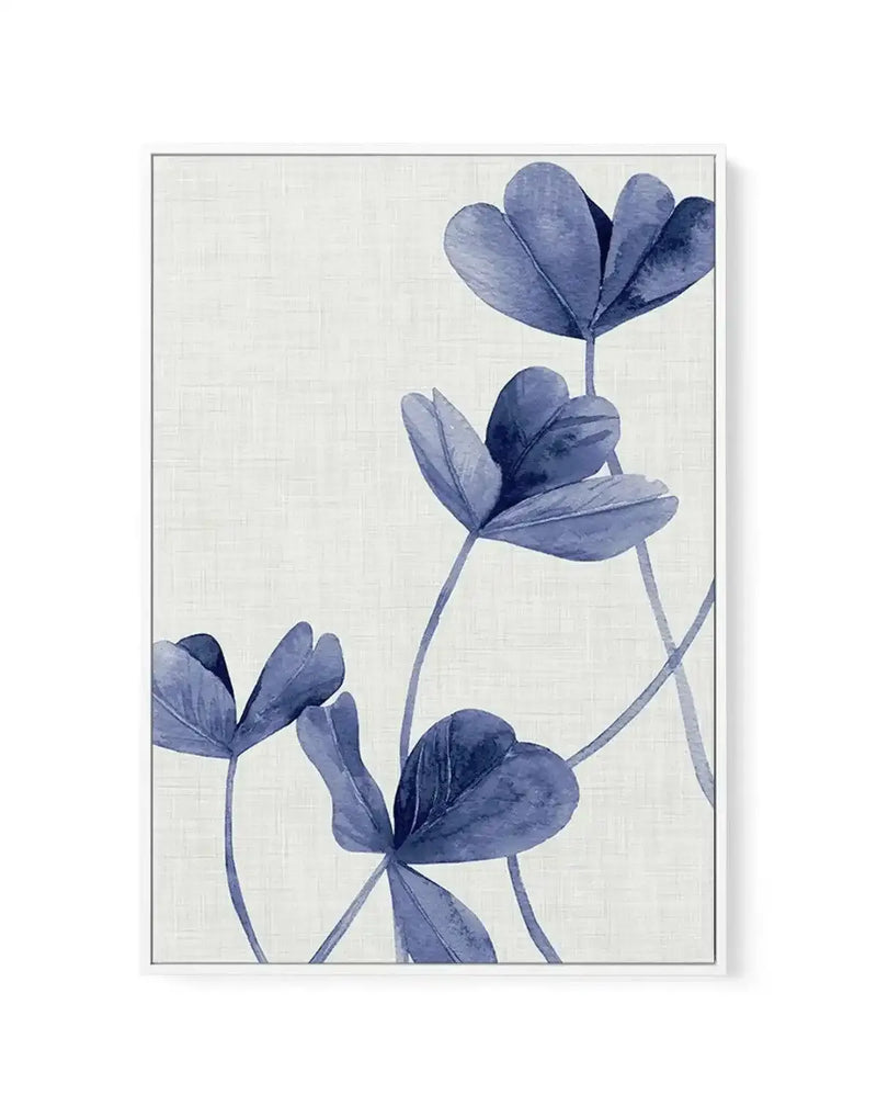 Framed canvas art print featuring three indigo blue flowers with delicate petals and thin stems against a cream textured background. The botanical illustration uses watercolor-style rendering with varying shades of blue-gray, creating depth and dimension. The canvas is mounted in a slim gray frame with a white border. The composition is vertical with flowers positioned at staggered heights, creating an elegant, minimalist arrangement.