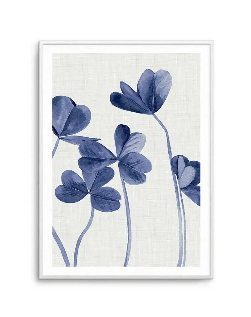 Watercolour art print featuring four three-leaf clovers with deep indigo blue petals and thin stems, on a textured cream background, displayed in a white frame with white border.