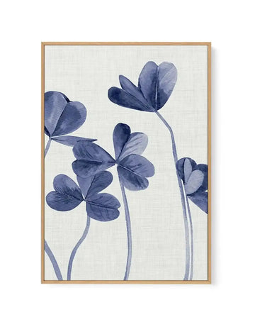 Framed canvas art print featuring watercolor-style blue flowers with delicate stems against a cream textured background. Four flowers in varying shades of indigo and slate blue are arranged vertically, with heart-shaped and rounded petals showing translucent watercolor effects. The artwork is set in a natural wood frame with a white border, displaying a botanical illustration with soft, minimalist aesthetic.