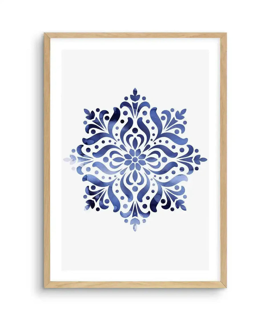 Watercolour art print featuring a symmetrical mandala-like design in varying shades of blue, from deep navy to lighter sky blue, with visible brushstroke and watercolour bleed textures, printed on fine art paper and displayed in a natural oak frame with white border.