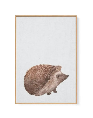 Framed canvas art print featuring a watercolor illustration of a hedgehog in profile, positioned in the lower center of the composition. The hedgehog has warm brown and tan quills with a lighter cream-colored face and underside. The background is a soft, pale off-white with subtle texture. The artwork is displayed in a natural wood frame with a white border surrounding the canvas.