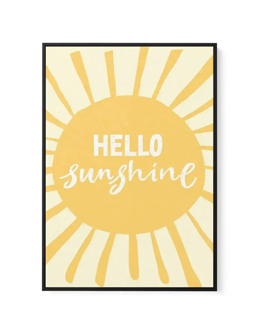 Framed canvas art print featuring a large golden-yellow sun with radiating rays against a pale cream background. White text reads "HELLO" in sans-serif font above "sunshine" in flowing script lettering, both centered within the sun. The canvas is mounted in a black frame with clean edges.