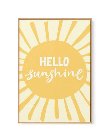 Framed canvas art print featuring a large golden-yellow sun with radiating rays in the center of a cream background. White text reads "HELLO" in sans-serif capitals above "sunshine" in flowing white script lettering, both centered on the sun. The canvas is set in a natural wood frame with a thin border.