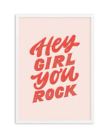 Art print featuring the phrase "Hey Girl You Rock" in bold, textured red lettering with a white outline, set against a soft blush pink background, displayed in a white frame with a white border.
