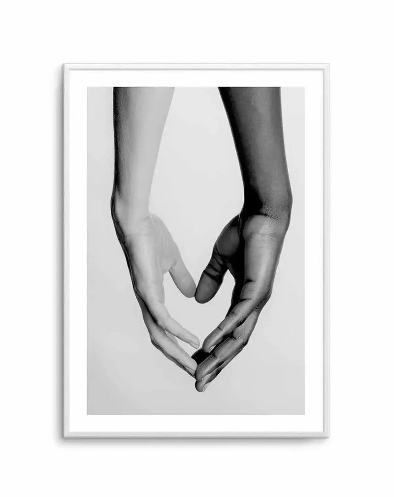 Framed black and white photograph of two hands, one light-skinned and one dark-skinned, forming a heart shape with their fingers, displayed in a white frame with white border. The hands are positioned vertically, with the wrists at the top and the fingertips meeting at the bottom to create the heart.