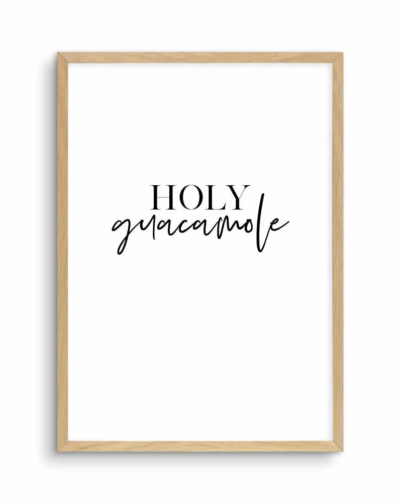 Framed art print with natural wood frame displaying text reading "HOLY" in serif capital letters followed by "guacamole" in flowing black script. White background with black typography. Simple, minimalist design suitable for kitchen or dining room décor.