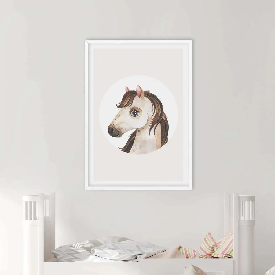 "Framed art print of a watercolour horse head displayed on a light grey wall above a white bunk bed in a child's bedroom. The print features a horse with light brown and cream fur, a dark brown mane, and large dark eyes, set against a plain white circular background. The white frame has a white border. The bed is made with a grey and white chevron patterned duvet and pillows with pink, green, and white stripes."