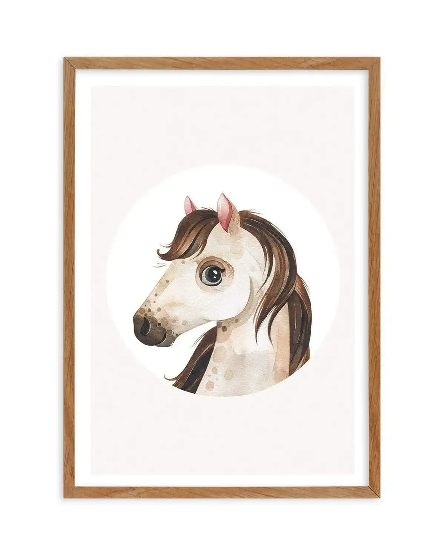 Watercolour art print featuring a charming horse head illustration in a natural oak frame with white border. The horse has a cream-coloured face with light brown speckles, a dark brown muzzle, and large, expressive dark eyes with a hint of blue. Its mane and forelock are a rich brown, and its ears are tipped with pink. The illustration is set against a clean white background within a circular crop.