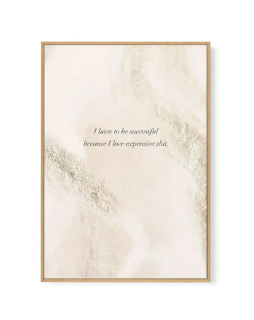 Framed canvas art print with light tan wooden frame featuring the text "I have to be successful because I love expensive shit" in dark gray italicized serif font centered on the canvas. The background displays an abstract watercolor-style texture in soft cream, beige, and pale gray tones with organic brushstroke marks and layered wash effects creating diagonal sweeping patterns across the composition. The overall aesthetic is minimalist and neutral with a matte finish.