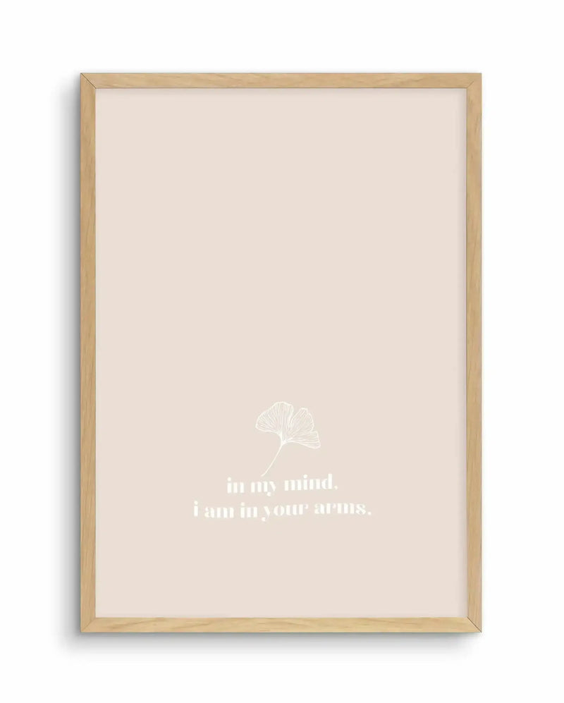 Framed art print with natural wood frame featuring a minimalist design on cream background. A delicate white line drawing of a ginkgo leaf appears in the center-lower portion of the print, accompanied by white serif text reading "in my mind. i am in your arms." The overall composition is simple and centered with generous cream-colored space surrounding the botanical illustration and typography.