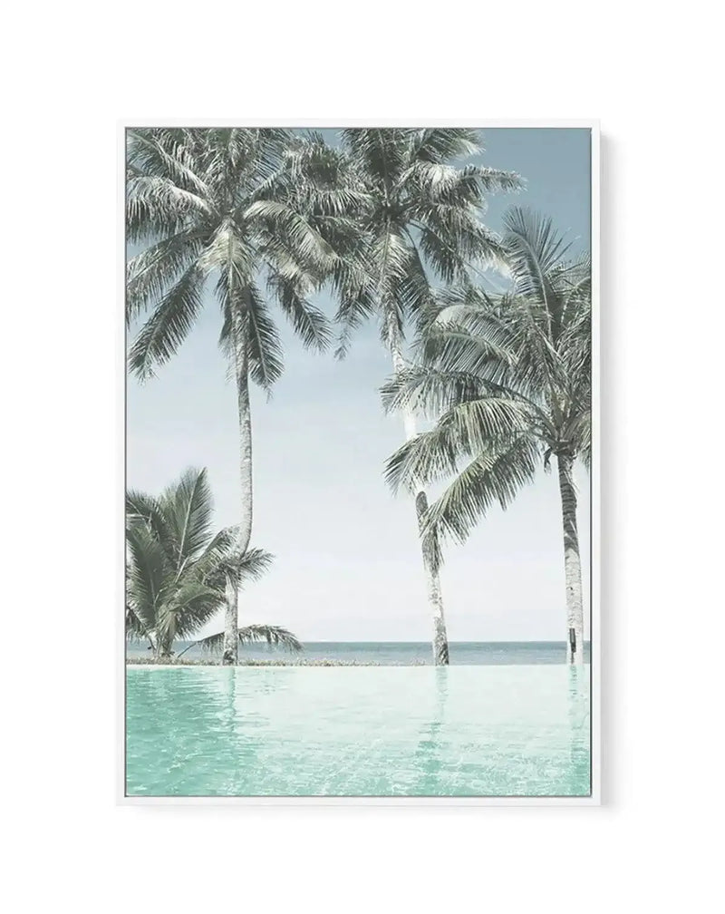 Framed canvas art print featuring a serene tropical beach scene with tall palm trees standing in shallow turquoise water. The composition shows multiple coconut palms with feathered fronds against a clear blue sky, with calm turquoise-green water in the foreground and a distant ocean horizon. The photograph has a soft, minimalist aesthetic with cool coastal tones. The canvas is mounted in a slim gray frame with white border.