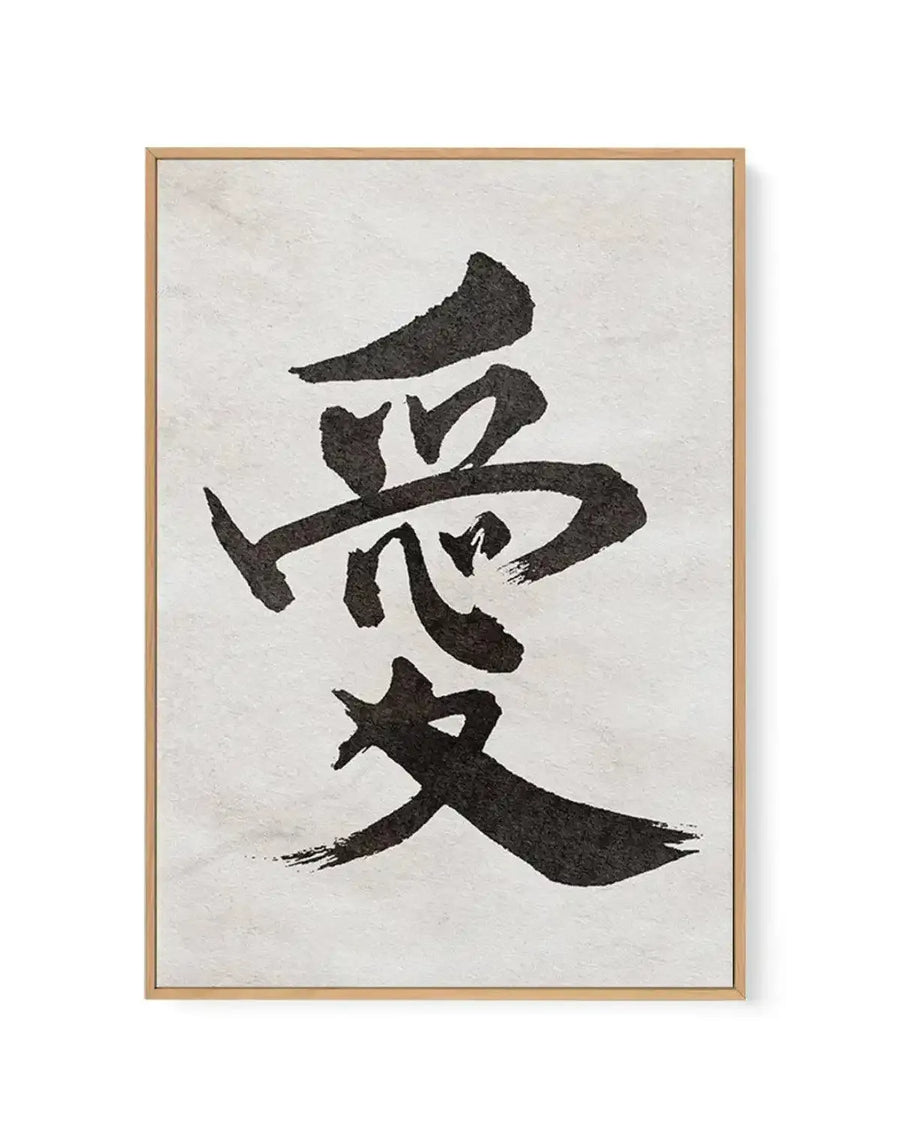 Framed canvas art print featuring Japanese calligraphy character for "love" rendered in bold black brushstrokes on a cream textured background. The character is composed of thick, expressive strokes with visible texture and ink variation, arranged vertically on the canvas. Natural wood frame with light tan finish surrounds the artwork. The cream-colored canvas creates contrast with the dark calligraphic marks, emphasizing the traditional aesthetic of the piece.