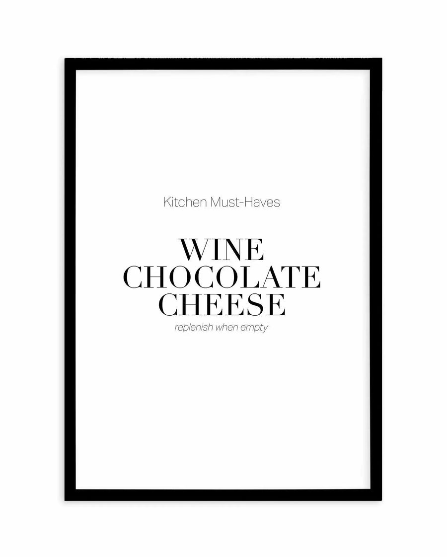 Black-framed art print with white background featuring centered text in a modern serif font. At the top in thin sans-serif: "Kitchen Must-Haves". Below in large bold serif letters: "WINE CHOCOLATE CHEESE". Beneath in smaller italic sans-serif: "replenish when empty". Clean, minimalist typographic design with black text on white, enclosed in a simple black frame with white border.