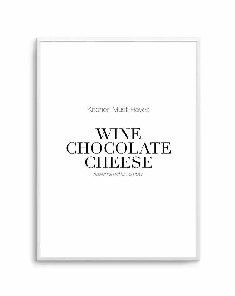 Framed art print with light gray border displaying centered text in a minimalist design. The header reads "Kitchen Must-Haves" in small, thin sans-serif font. Below that, the words "WINE CHOCOLATE CHEESE" appear in large, bold serif typeface in black. Underneath, italicized text in gray reads "replenish when empty." The background is off-white, and the entire piece is mounted in a white frame against a plain white background.