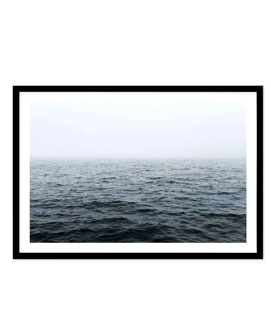Framed photograph of a calm, dark blue ocean under a hazy, light grey sky, printed on fine art paper and displayed in a black frame with white border.