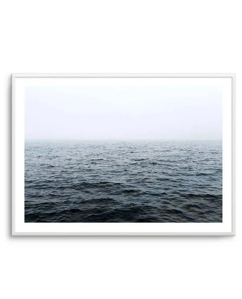 Framed photography art print of a moody ocean scene with a white frame and white border. The composition features dark, choppy water filling the bottom two-thirds of the frame, with a hazy, light grey sky meeting the horizon.