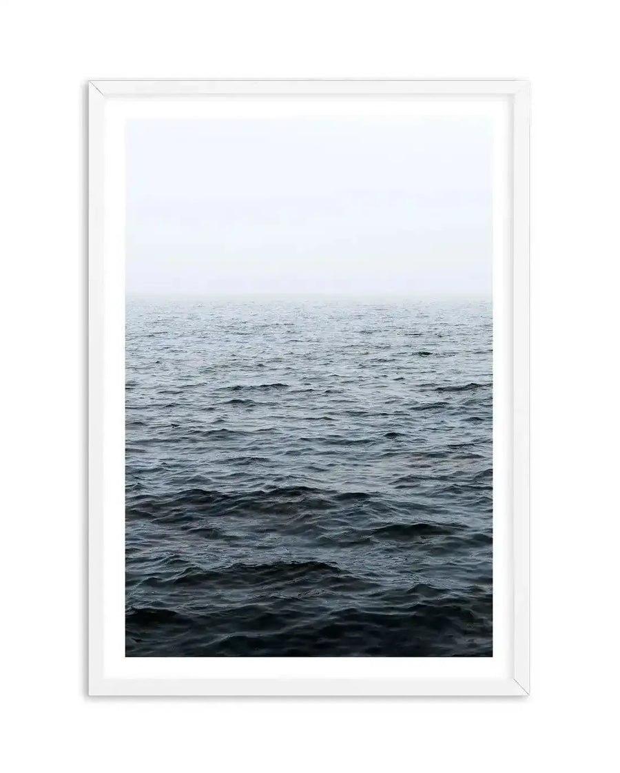Framed photography art print featuring a minimalist seascape with a dark, choppy ocean meeting a hazy, light grey sky at the horizon, displayed in a white frame with white border.