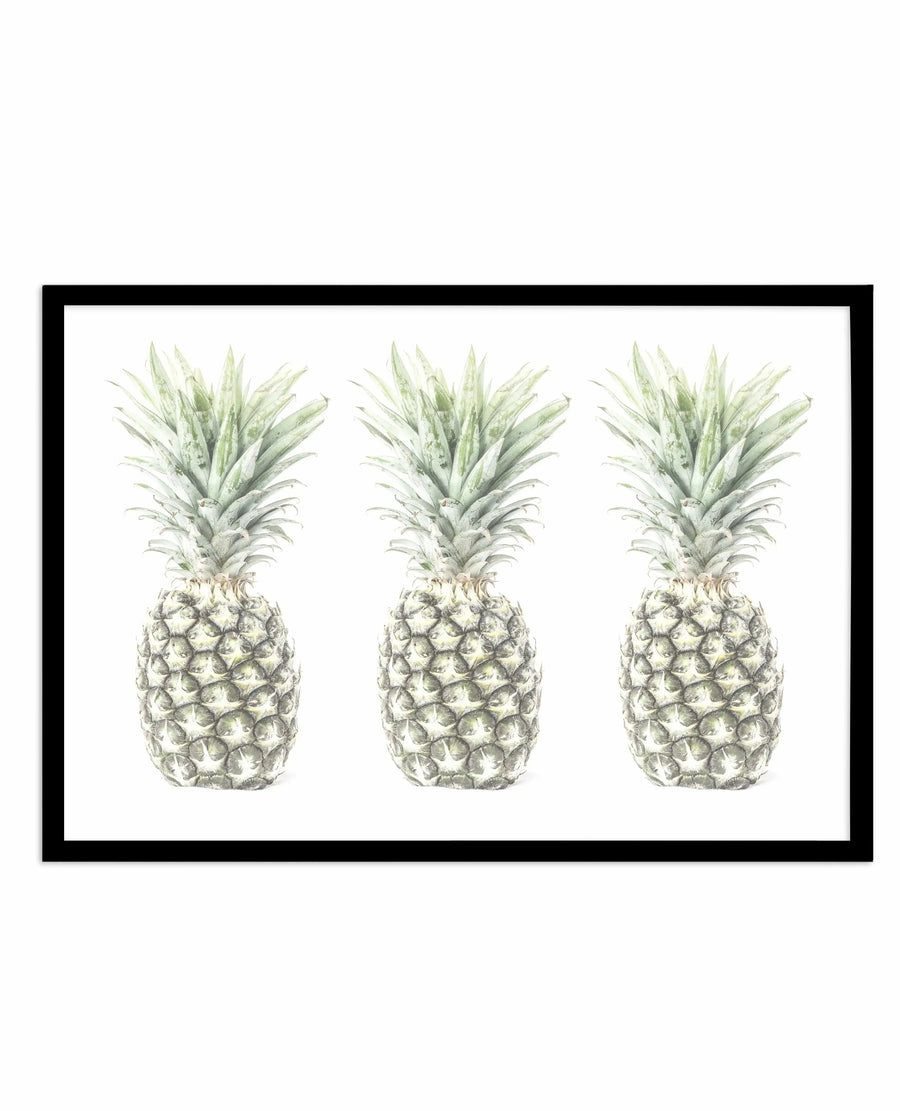 Three pineapples rendered in detailed botanical illustration style with muted sage green and cream tones, displayed horizontally against a white background in a black frame with white border. The artwork features fine line work and subtle shading that captures the textured surface of the fruit and delicate leaves of each pineapple.