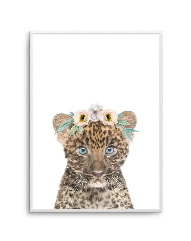 Watercolour art print featuring a baby leopard cub wearing a flower crown, printed on fine art paper and displayed in a white frame with white border. The leopard cub has blue eyes and soft brown fur with dark spots, and the flower crown includes pale pink, cream, and white flowers with light green leaves.
