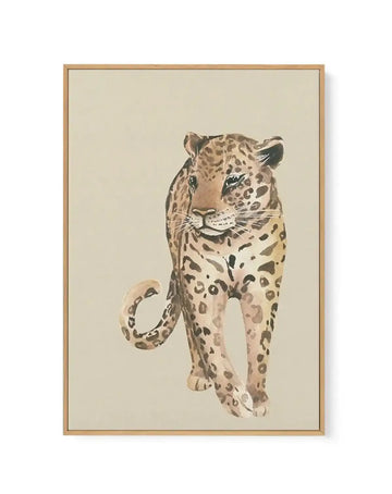 Watercolor painting of a leopard walking forward against a cream background, framed in natural wood. The leopard features warm tan and beige tones with dark brown rosette spots and markings throughout its body, face, and curved tail. The artistic style uses soft watercolor washes creating a naturalistic yet painterly effect. The wooden frame has a simple, understated design with a white border around the canvas artwork.