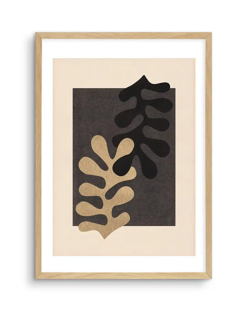 Abstract art print featuring two overlapping organic leaf-like shapes in black and metallic gold against a dark grey background, with a natural wood frame and white border.