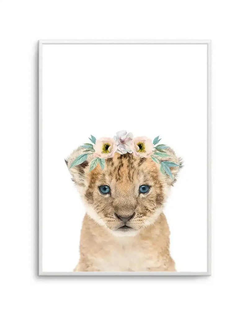 Watercolour art print featuring a cute baby lion cub with bright blue eyes, wearing a delicate flower crown with soft pink and white blooms and sage green leaves, printed on fine art paper and displayed in a white frame with white border