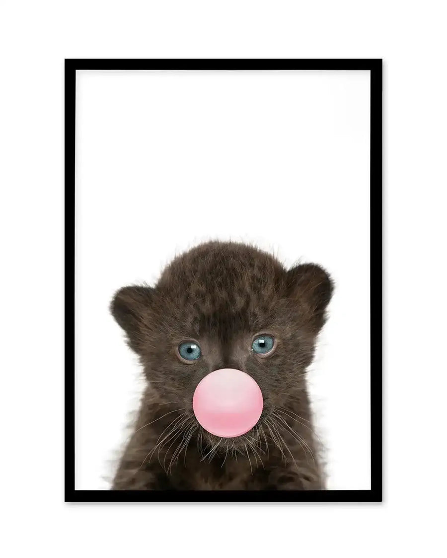 Art print featuring a young leopard cub with dark gray-brown fur and bright blue-green eyes, blowing a large bubble gum bubble in soft pink. The cub's face fills most of the composition against a clean white background, with visible whiskers and pointed ears. The image has a photorealistic style with a playful, whimsical quality. The print is displayed in a black frame with a white border.