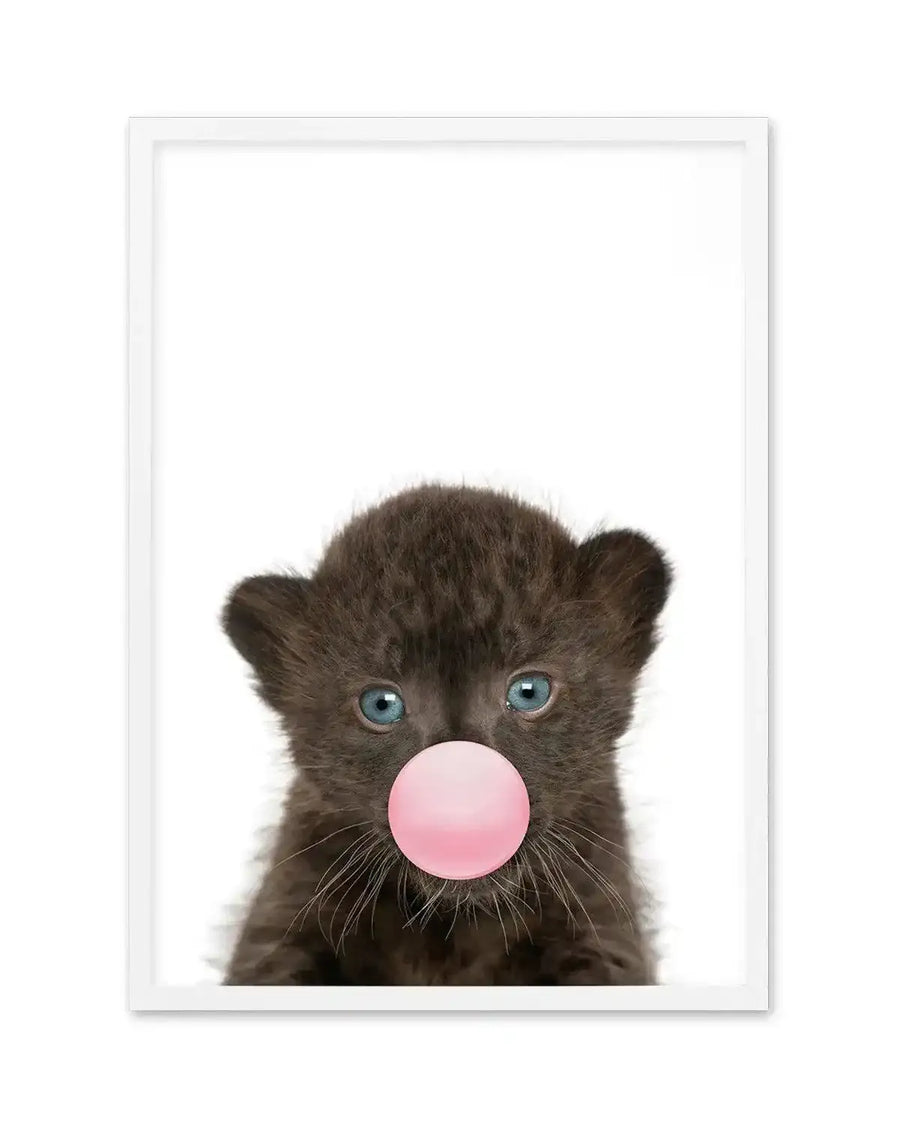 Black leopard cub with bright blue eyes facing forward against a white background, blowing a large bubble gum pink bubble. Photograph-style art print with white frame and white border, positioned vertically in portrait orientation.