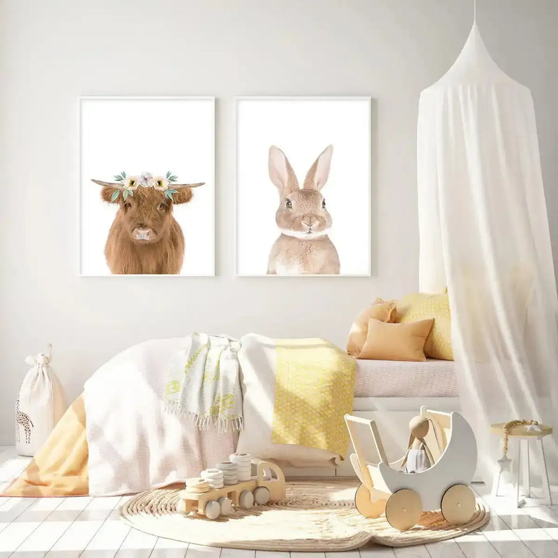 Nursery:
"Two framed art prints displayed side-by-side above a bed in a bright nursery. The left print features a fluffy brown Highland cow wearing a floral crown, and the right print features a brown bunny with large ears, both on a white background with white frames. The room includes a white bed with yellow and white bedding, a white canopy, a round woven rug, and wooden toys."
