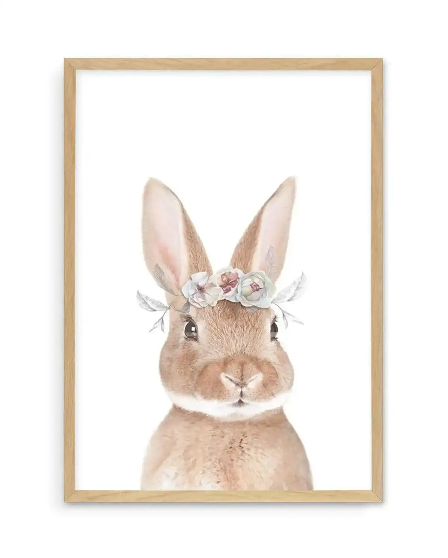 Watercolour art print featuring a sweet brown bunny with soft fur and large ears, wearing a delicate flower crown with white, blush pink, and pale blue blossoms and grey-green leaves, displayed in a natural oak frame with white border.