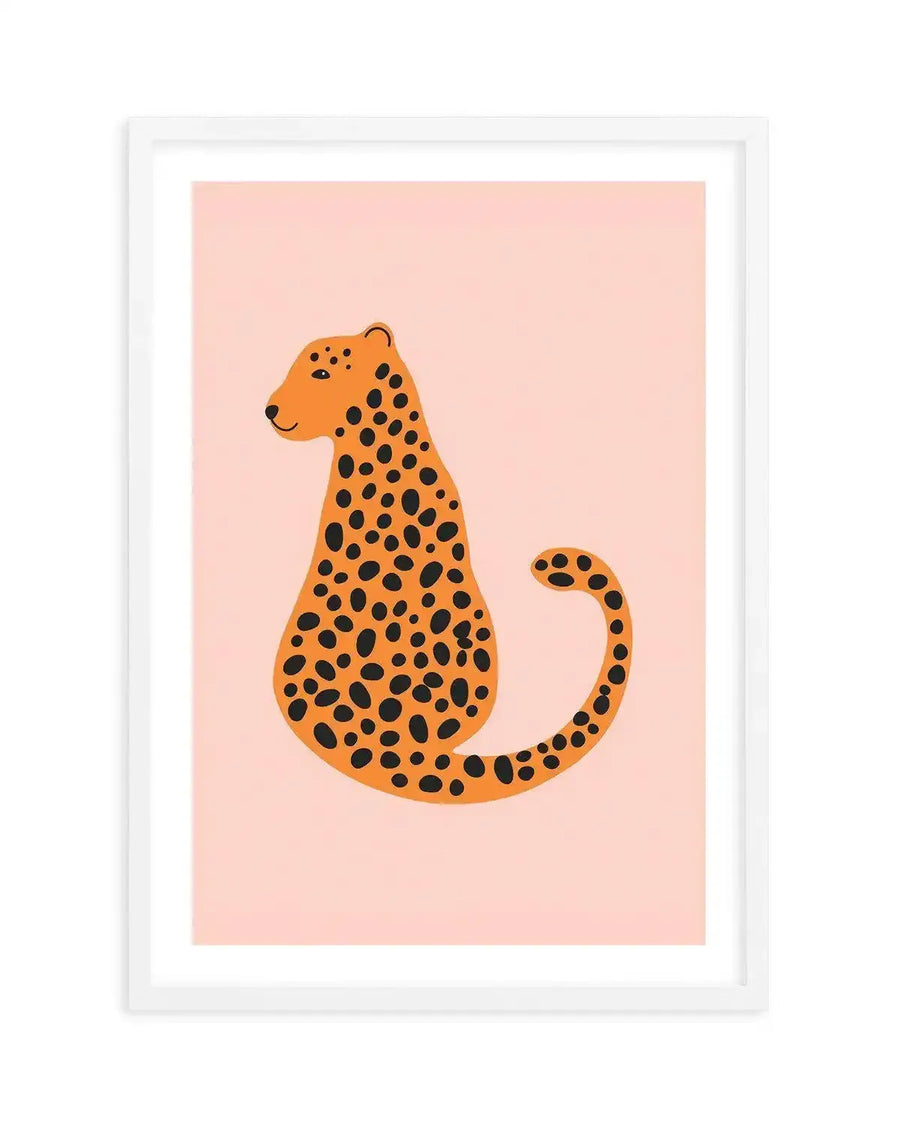 Art print featuring a stylized illustration of a cheetah sitting on a pale pink background, with a white frame and white border. The cheetah is depicted in a warm orange hue with numerous black spots of varying sizes, and has a gentle expression with small black eyes and a curved smile. Its tail curls upwards to the right.