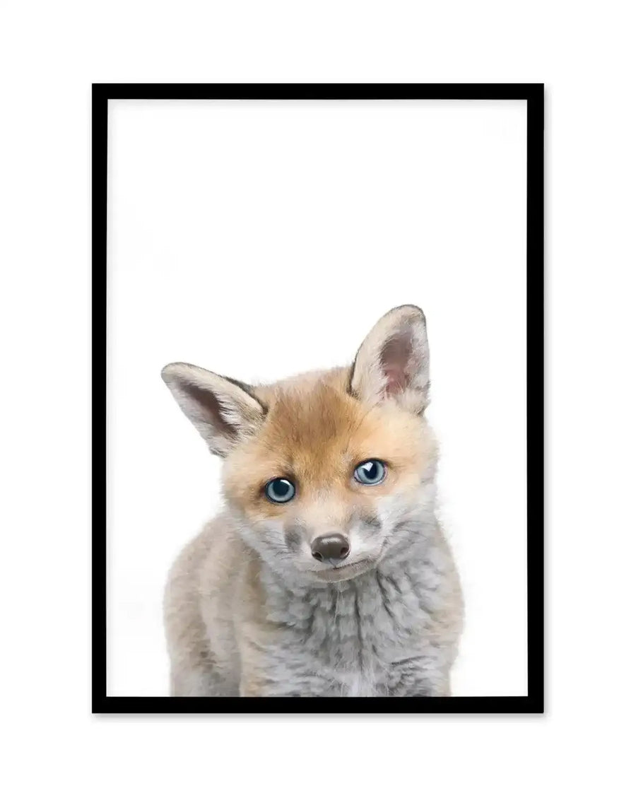 Framed photography art print featuring a close-up of a baby fox with bright blue eyes and soft, fluffy light brown and grey fur, looking directly at the viewer, with a black frame and white border.