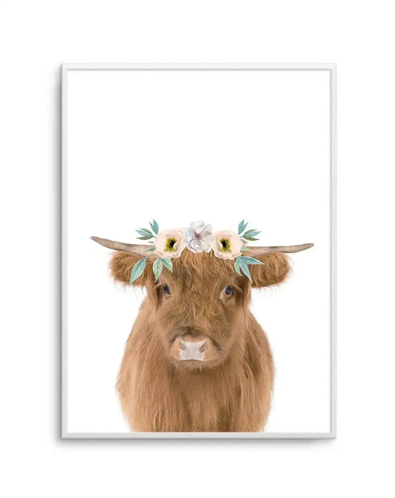 Watercolour art print featuring a fluffy brown Highland cow with small horns, wearing a delicate flower crown with white, pale yellow, and pink blooms, and green leaves, on a clean white background, displayed in a white frame with a white border.