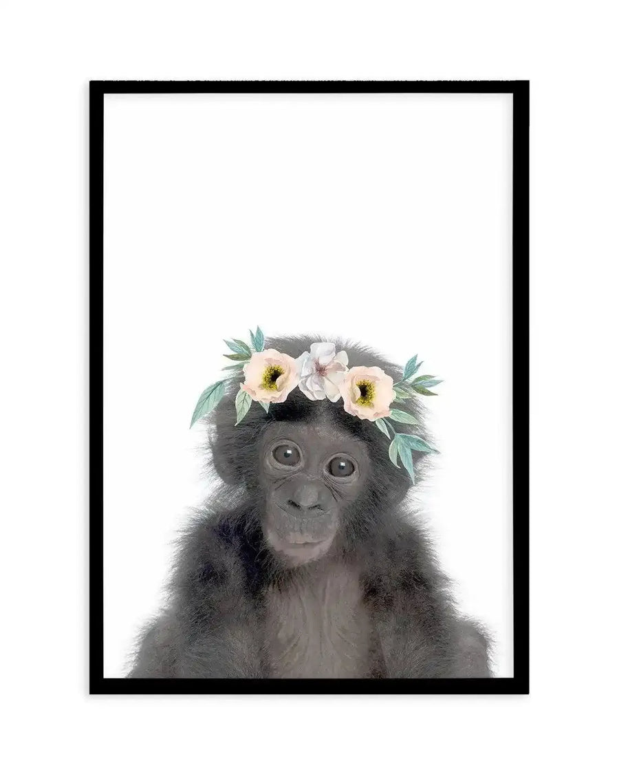 Watercolour art print featuring a baby chimpanzee looking directly at the viewer, wearing a delicate floral crown with pale pink and white flowers and soft green leaves, printed on fine art paper and displayed in a black frame with white border.