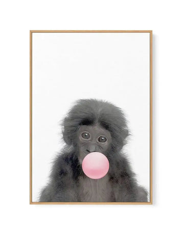 Framed canvas art print featuring a young black monkey with fluffy dark gray fur and large expressive eyes blowing a bright pink bubble. The monkey's face is centered against a clean white background, displaying a playful, whimsical expression. The artwork is presented in a natural wood-tone frame with a white border, creating a simple, minimalist composition that emphasizes the charming subject matter.