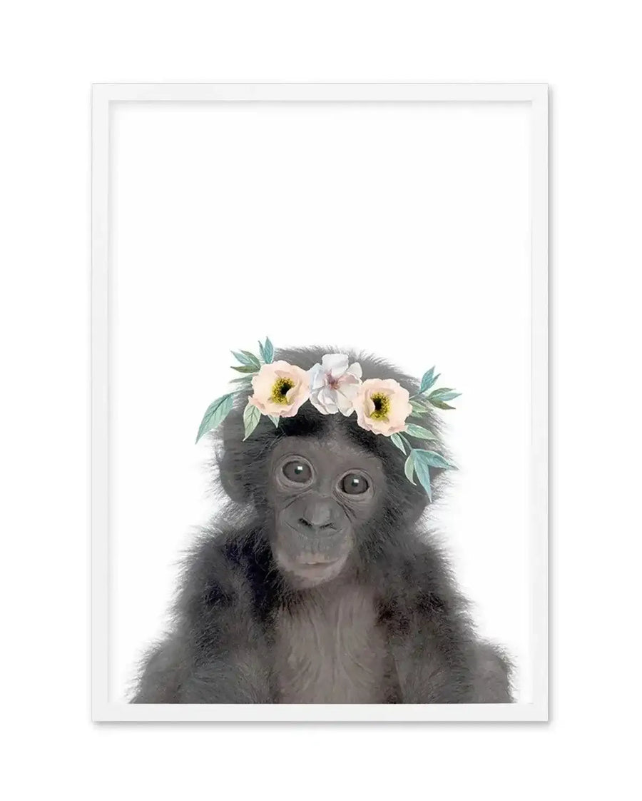 Watercolour art print featuring a baby chimpanzee wearing a flower crown, printed on fine art paper and displayed in a white frame with white border. The chimpanzee has dark grey fur and large, dark eyes, looking directly at the viewer with a gentle expression. The flower crown consists of pale yellow and white blossoms with soft green leaves.